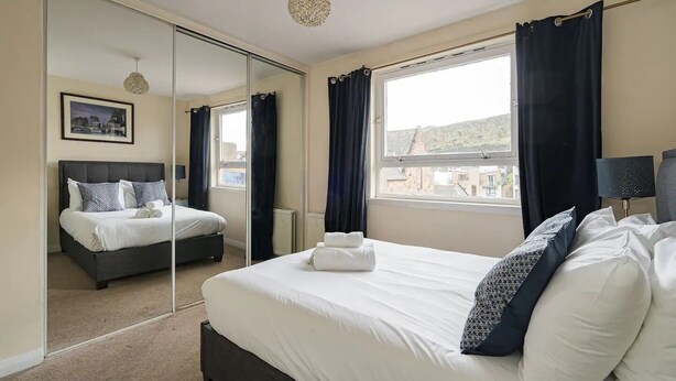 Une chambre d’hôtel avec un grand lit, un miroir, une fenêtre avec des rideaux et une vue sur la ville.