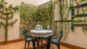 A small outdoor patio with a round table and chairs, surrounded by a lattice wall covered with climbing plants and flowers.