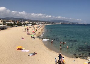 A wide sandy beach with clear blue water, umbrellas, and people enjoying the seaside.