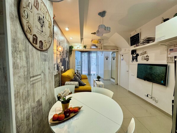 A modern living room with a round dining table, a sofa, and a TV mounted on the wall.