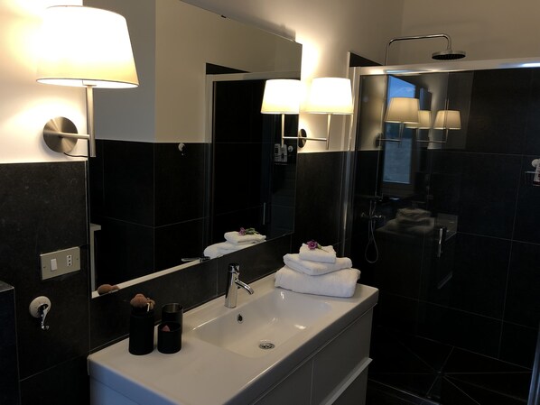 A modern bathroom with a large mirror, two wall-mounted lights, a sink, and a shower area.