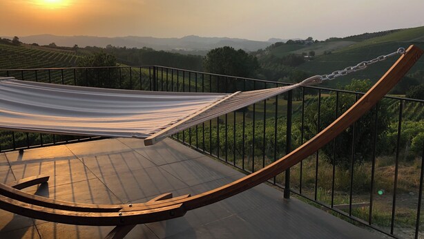 Eine Hängematte auf einem Balkon mit Blick auf Weinberge und ferne Hügel.