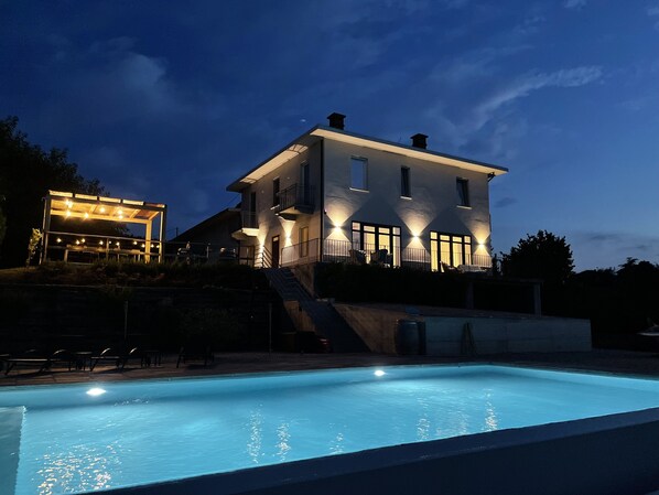 Una casa grande con piscina, un área exterior techada y una escalera que lleva a la casa.