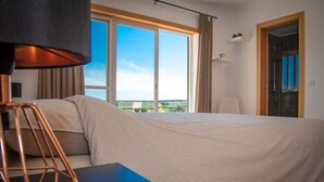 A hotel room with a large bed, a desk, a lamp, and a view of the outdoors through a large window. - Spacious & new holiday home for max. 6 people (Aljubarrota)