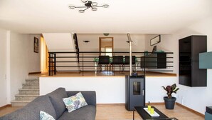 A modern living room with a grey sofa, a glass coffee table, and a staircase leading to a dining area with black chairs. - Spacious & new holiday home for max. 6 people (Aljubarrota)