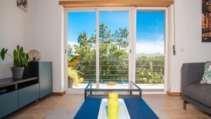 A modern living room with a sliding glass door leading to a balcony, a blue sofa, a small table with candles, and a potted plant. - Spacious & new holiday home for max. 6 people (Aljubarrota)