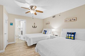 A hotel room with two beds, a ceiling fan, a bathroom with a toilet and sink, and a door leading to another room.