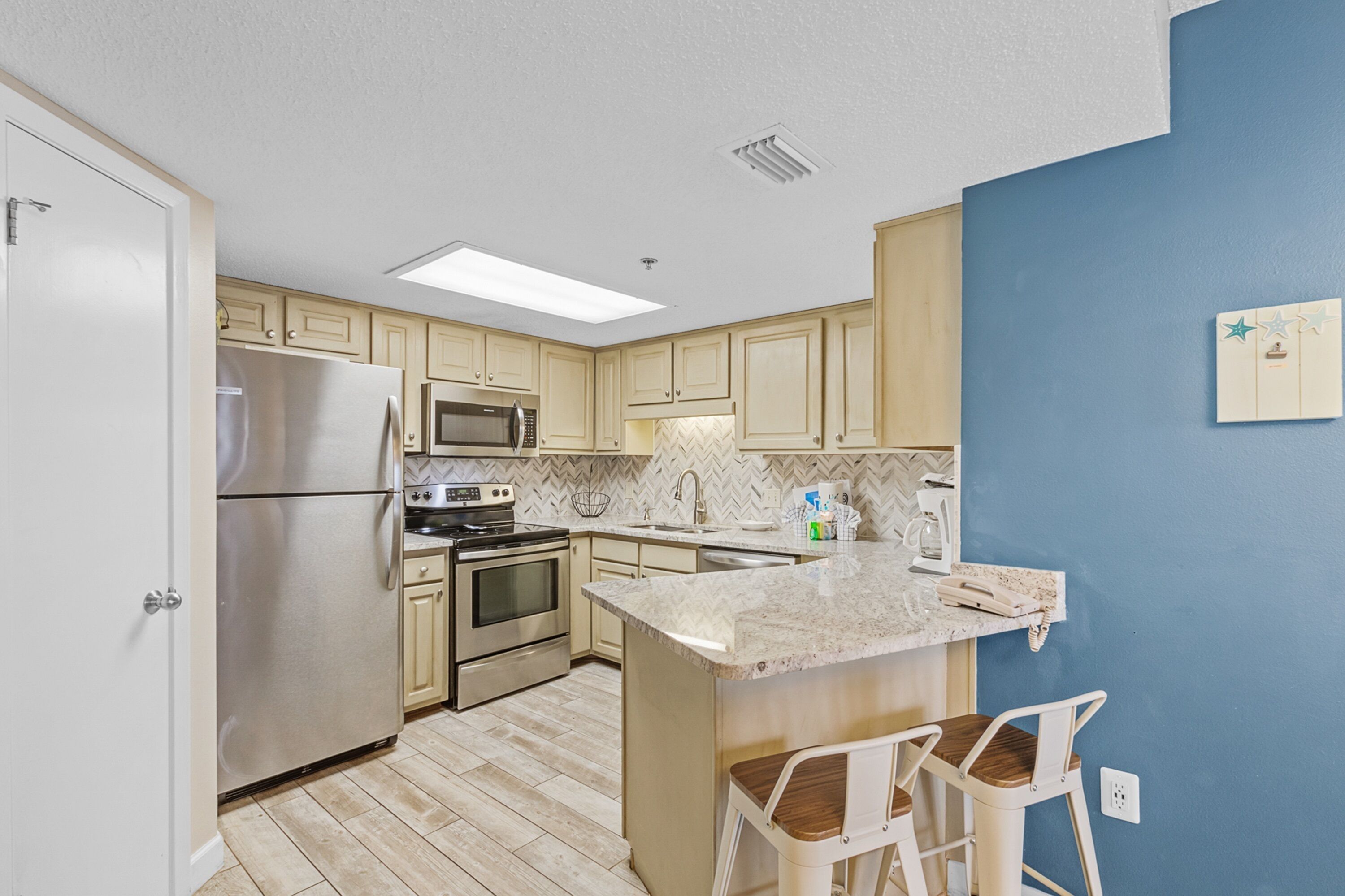 A modern kitchen with light wood cabinets, stainless steel appliances, a herringbone backsplash, and a blue accent wall.