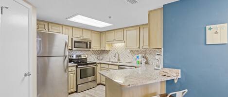 A modern kitchen with light wood cabinets, stainless steel appliances, a herringbone backsplash, and a blue accent wall.