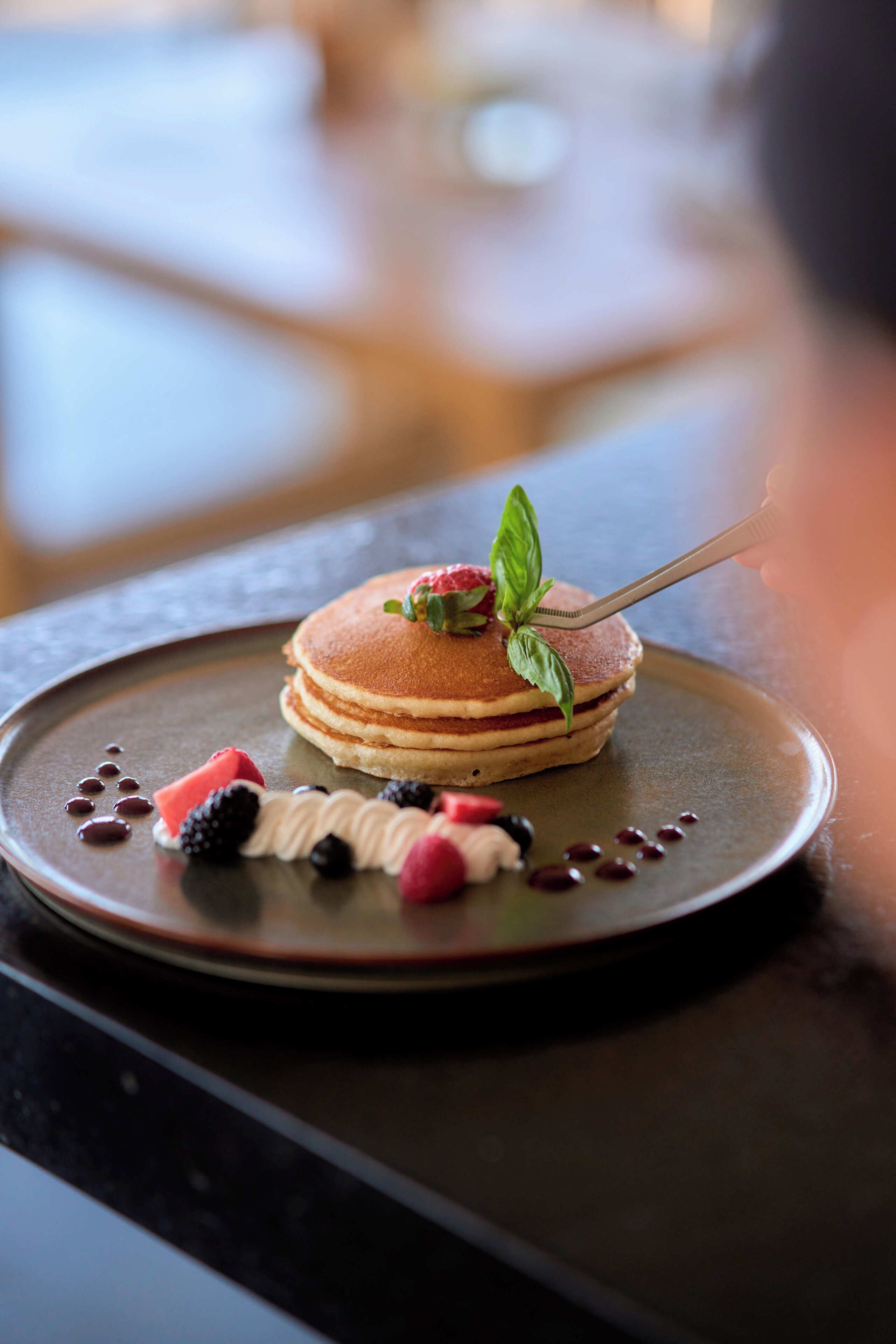 Une pile de crêpes garnie de fruits rouges et de crème fouettée, présentée sur une assiette.