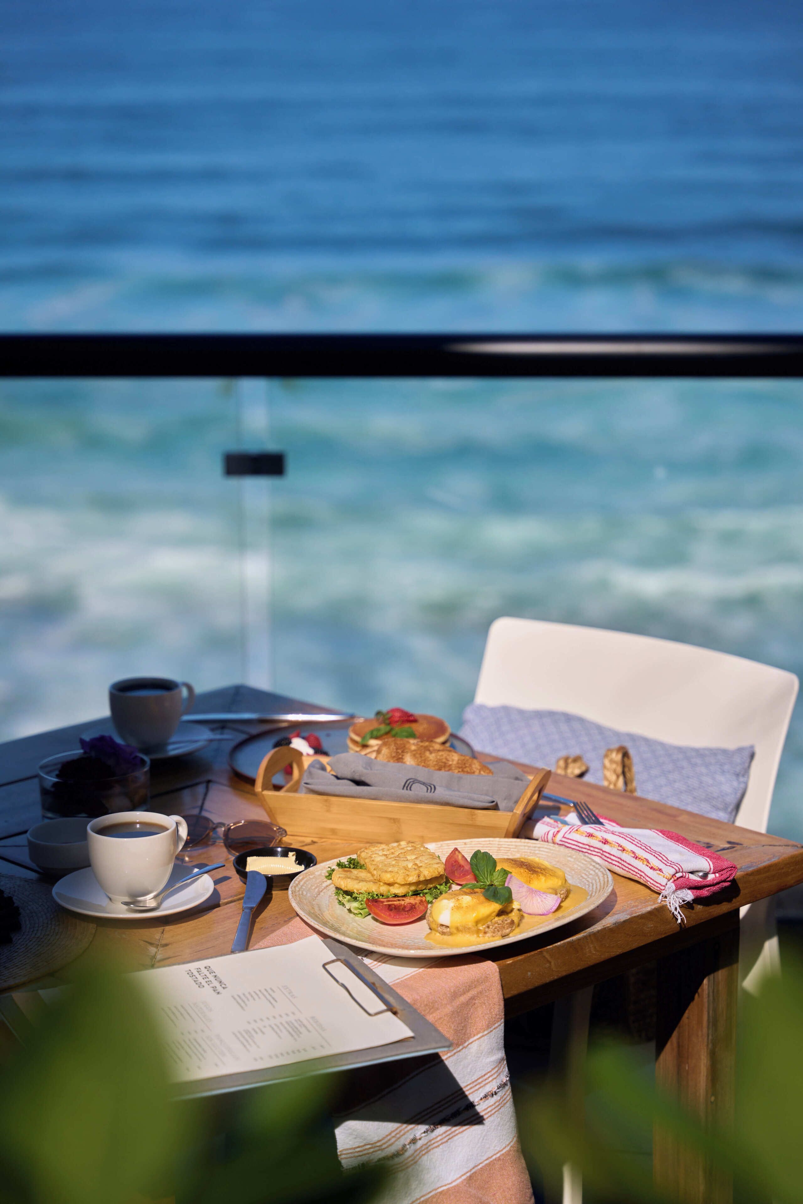 Una mesa con comida, una taza de café y un menú, con vista a un cuerpo de agua.