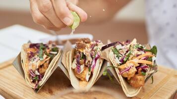 Tres tacos sobre una tabla de madera, con una mano exprimiendo un limón.