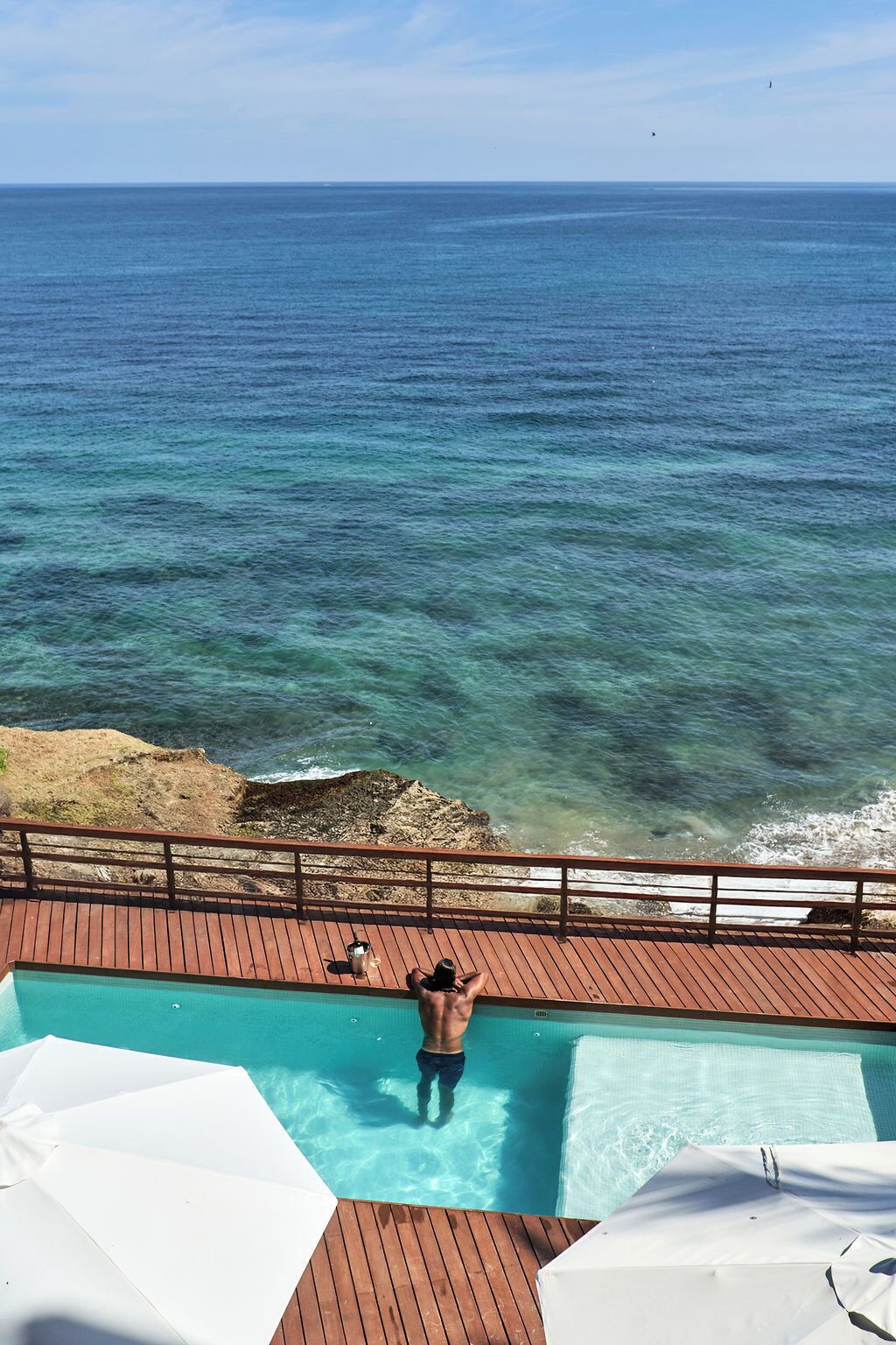 A man in a swimming pool with a view of the ocean.