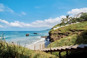 Vista costeira com escadaria de madeira que leva a uma casa com vista para a praia.