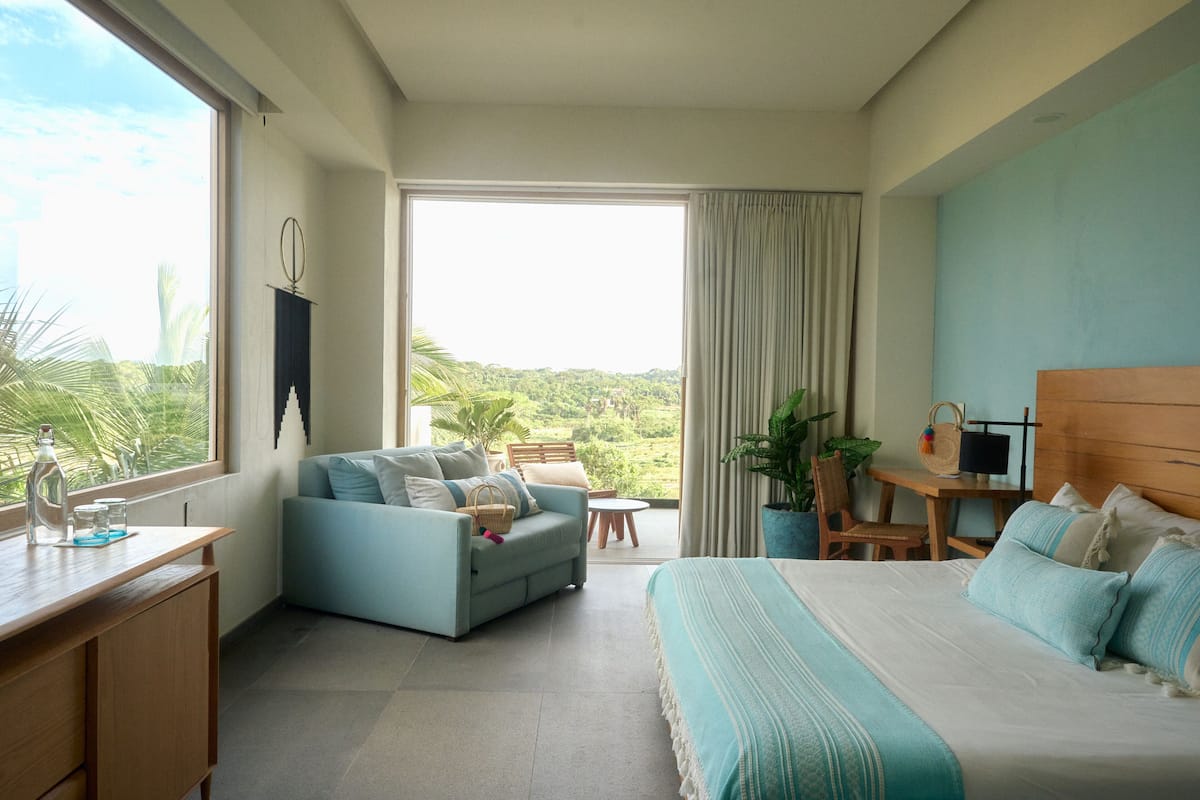 A hotel room with a bed, a sofa, a desk, and a view of the outdoors.