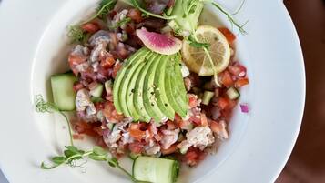 Une assiette blanche contenant une salade de fruits de mer, des tranches d’avocat, un citron et du concombre.