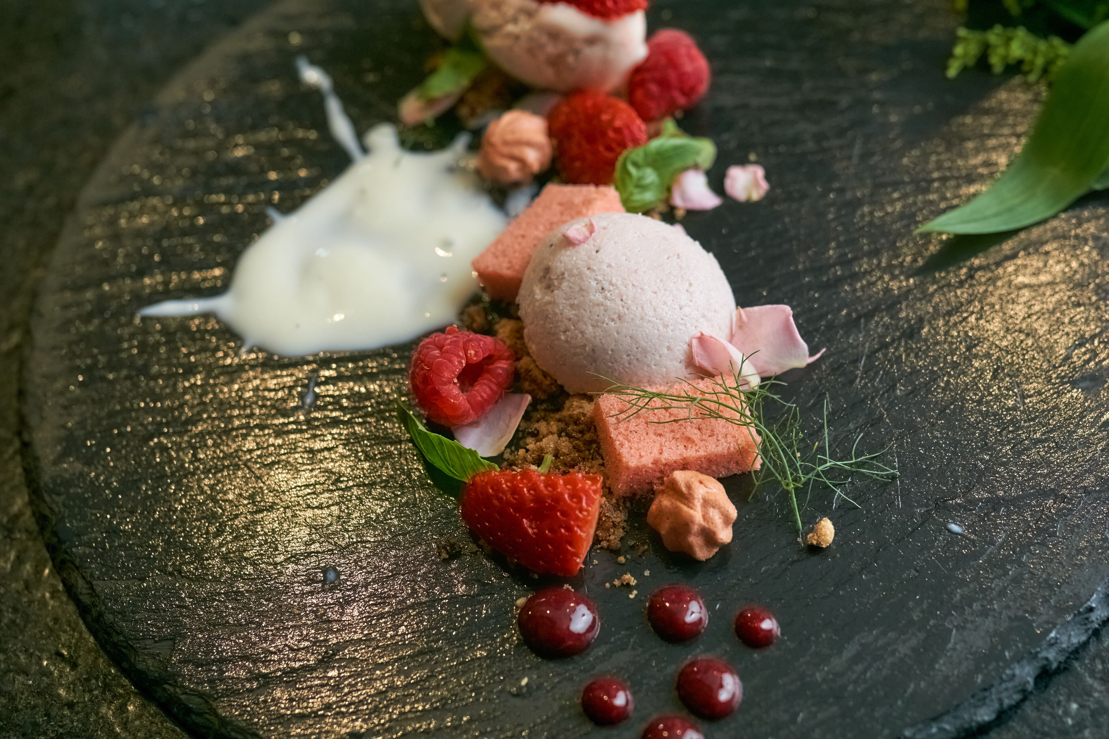 A dessert with strawberries, raspberries, and a dollop of cream on a slate plate.
