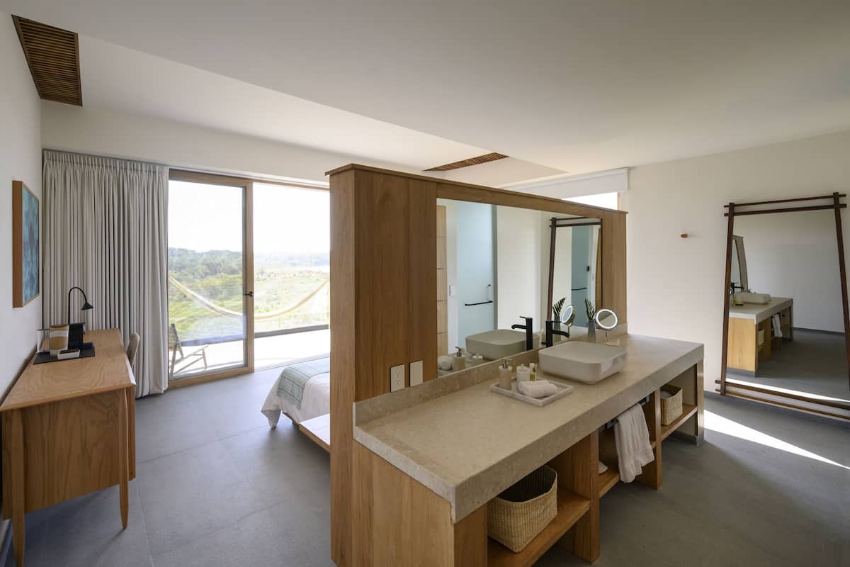 A modern bathroom with a large mirror, wooden vanity, and a view of the outdoors.