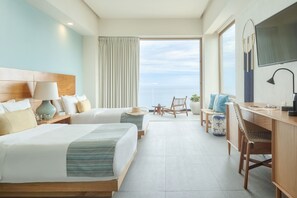 Quarto de hotel com duas camas, uma escrivaninha, uma cadeira, uma televisão e vista para o mar.