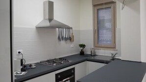Une cuisine moderne équipée d’un four encastré, d’une cuisinière à gaz et d’une fenêtre avec des stores.