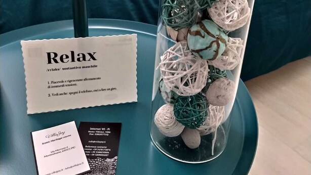 Un vase en verre orné de boules décoratives, posé sur une table de couleur turquoise, une carte portant l’inscription « Détendez-vous » et une carte de visite.