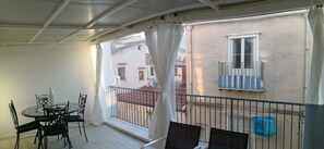 Un balcón con mesa y sillas, vista a edificios vecinos y una barandilla.