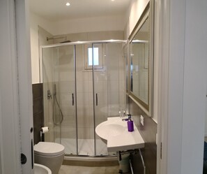 Un baño moderno con ducha de vidrio, lavamanos blanco y un espejo grande.