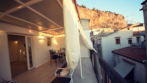 Ein Balkon mit Essbereich, Blick auf eine steile Klippe und ein Gebäude mit Ziegeldach.