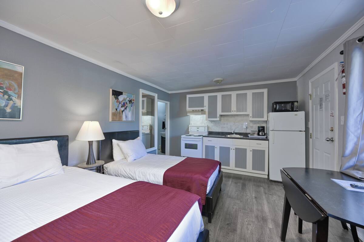 A hotel room with two beds, a desk, a microwave, and a kitchenette.