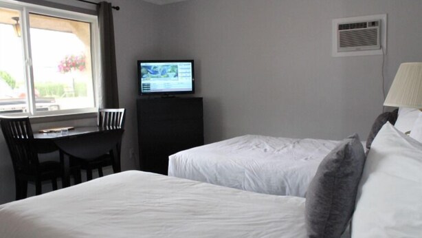 Une chambre d’hôtel avec deux lits, un bureau, une chaise, une télévision et une fenêtre.