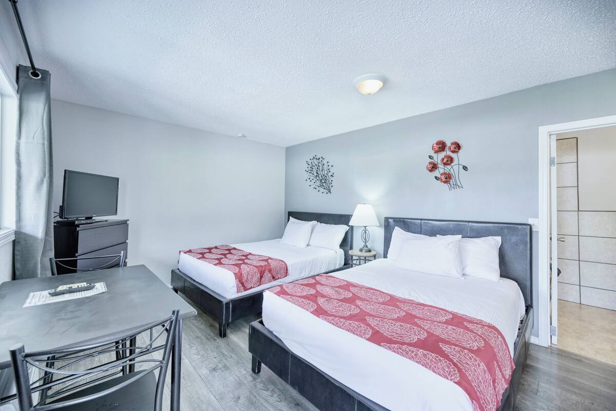 A hotel room with two beds, a desk, a chair, a television, and a door leading to another room.