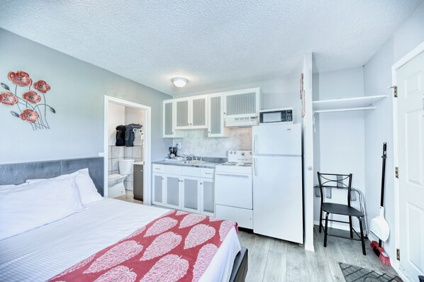 A compact hotel room with a bed, kitchenette, and a bathroom.