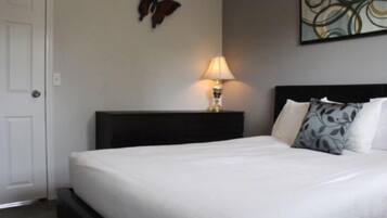 Een net opgemaakt bed met witte lakens, een donker hoofdbord en een lamp op het nachtkastje.