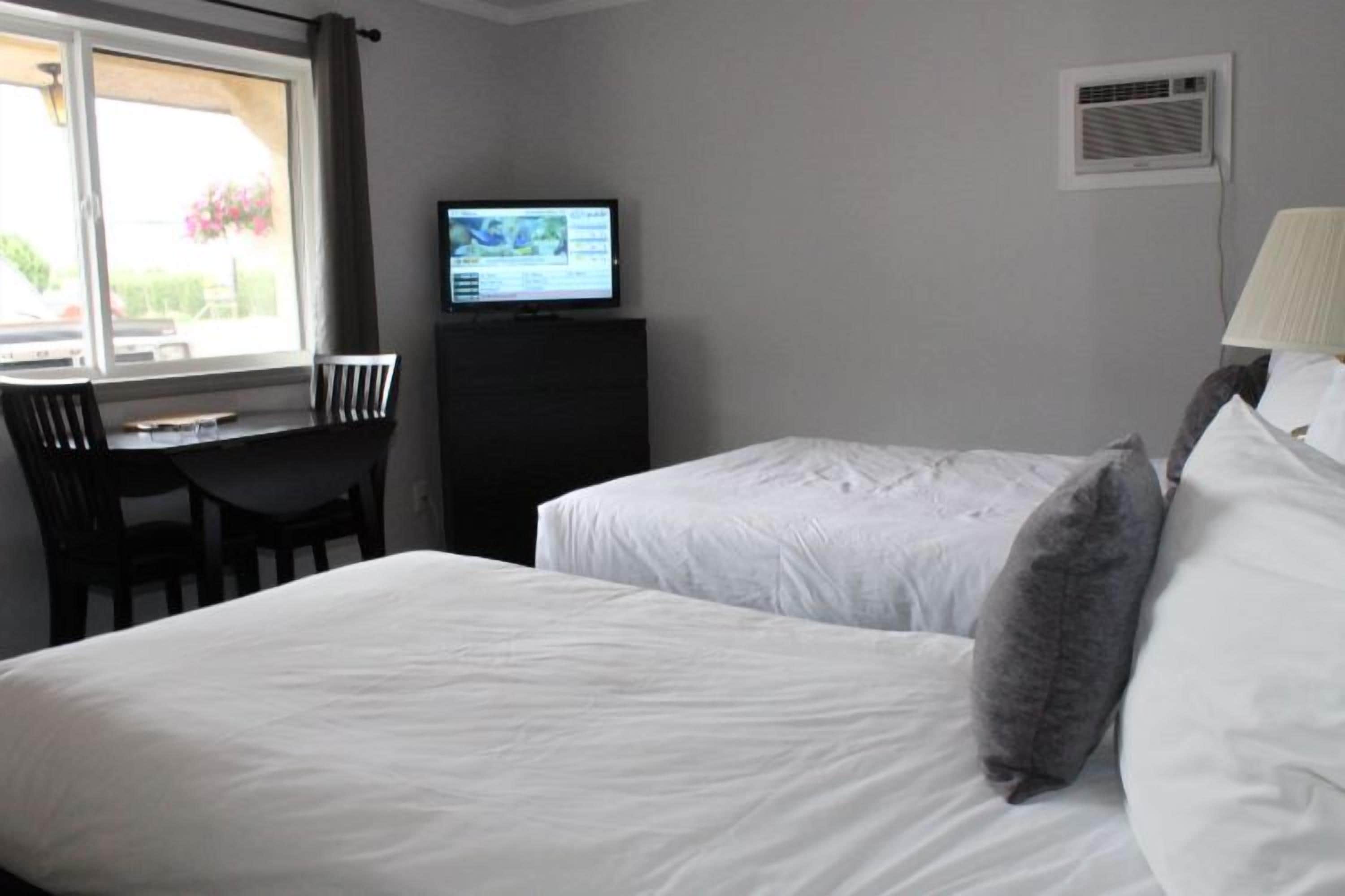 Habitación de hotel con dos camas, un escritorio, una silla, un televisor y una ventana.
