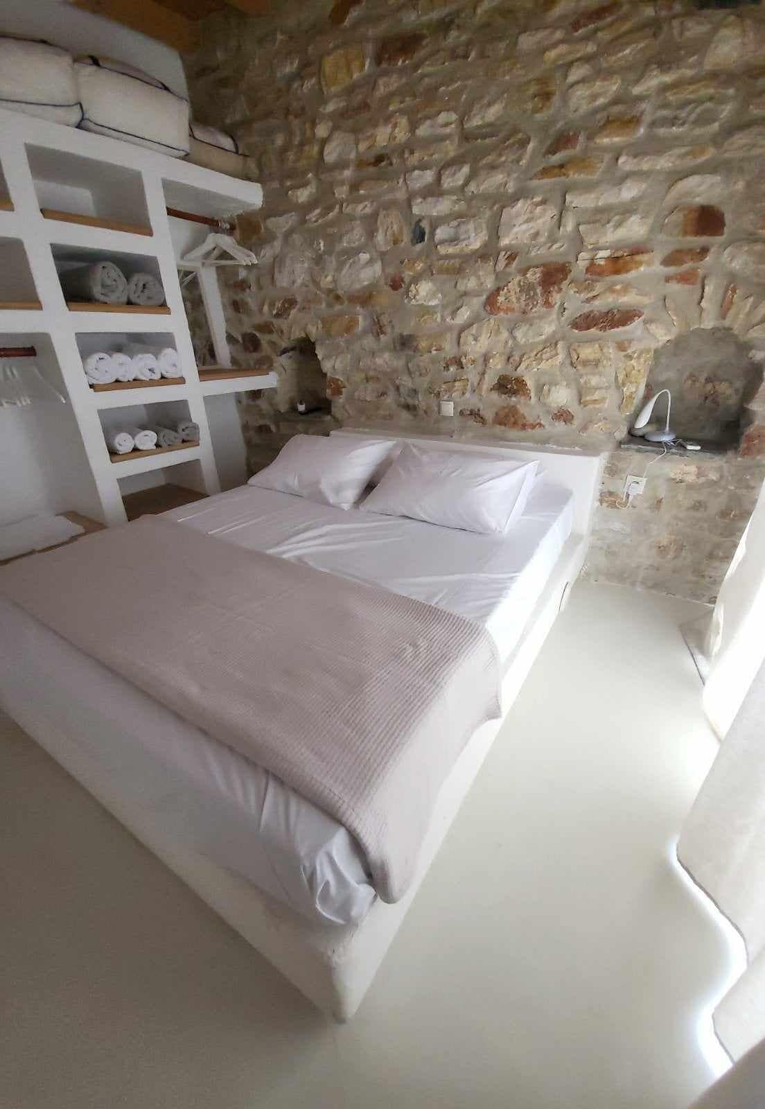 A bedroom with a stone wall, a bed with white linens, and a wooden shelf with towels.