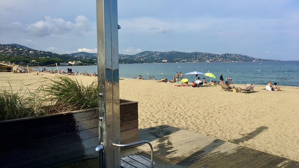 Ein Strand mit einer Holzterrasse und einer Metallkonstruktion, vermutlich einem Rettungsschwimmturm, mit Blick auf das Meer.