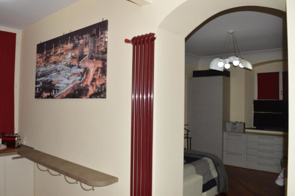 Una sala de estar con una cortina roja, un cuadro y una zona de comedor con un armario blanco y una silla roja.