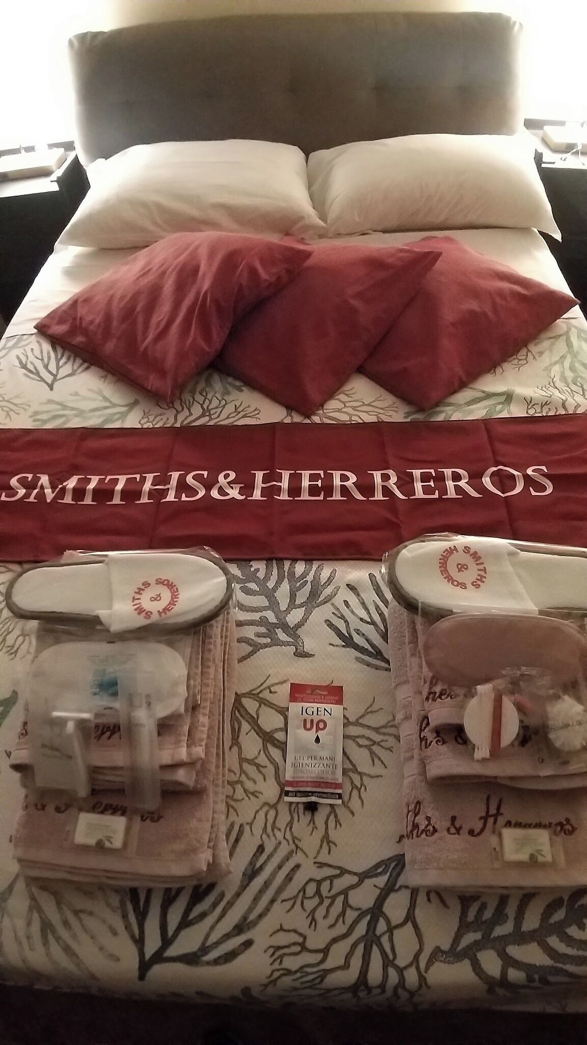 Un lit d’hôtel avec un oreiller rouge et blanc, une couverture rouge et un porte-serviettes contenant des articles de toilette.