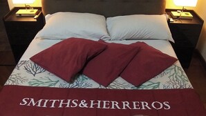 A hotel room with a bed, two nightstands, a wall clock, and a painting. - SMITHS & HERREROS (Codie CIN IT010025C2Q2M67QJW) (Genova)