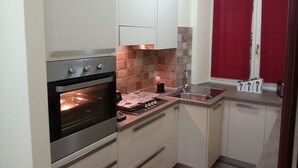 A compact kitchen with a built-in oven, a sink, and a red cabinet door. - SMITHS & HERREROS (Codie CIN IT010025C2Q2M67QJW) (Genova)