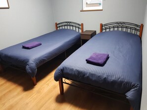 Two single beds with wooden frames and blue bedding, a small bedside table, and a framed picture on the wall.