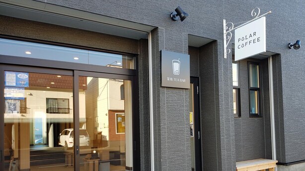 A building with a glass entrance, a sign for "Polar Coffee", and a bench outside. - Ak Star (Furano)
