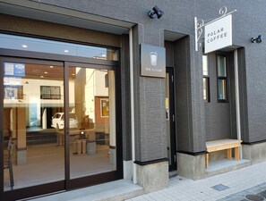 A building with a glass entrance, a sign for "Polar Coffee", and a bench outside.