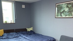 A bedroom with a bed, a gray sofa, a window with a view, and a plant on the wall. - Ak Star (Furano)