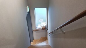 A wooden staircase with a metal handrail leading to a landing with a window. - Ak Star (Furano)