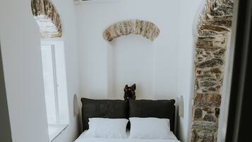 A bedroom with a bed, a chandelier, a stone wall, and a window.
