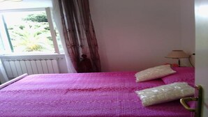 Une chambre avec un lit recouvert d’une couverture violette, une fenêtre avec des rideaux et une lampe sur une table.