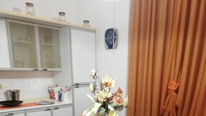 Un coin repas avec une table dressée pour deux personnes, un vase rempli de fleurs et, au fond, une cuisine.