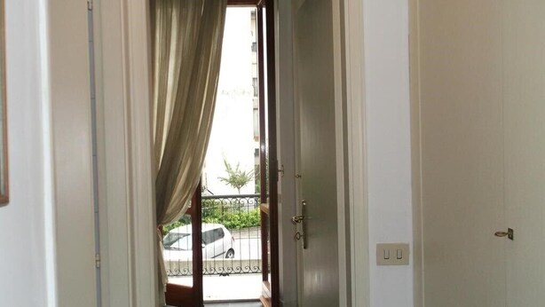 Un couloir menant à un balcon d’où l’on peut admirer une voiture garée et la verdure environnante.