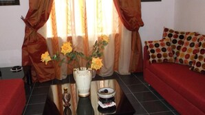 Une pièce avec un canapé, une table ornée d’un vase de fleurs et une fenêtre avec des rideaux.